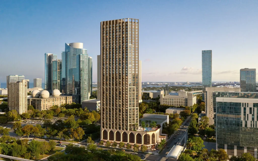 Un rascacielos alto y decorado, situado en la esquina de la Primera con la Quinta, se alza entre otros edificios de gran altura y árboles en un paisaje urbano.