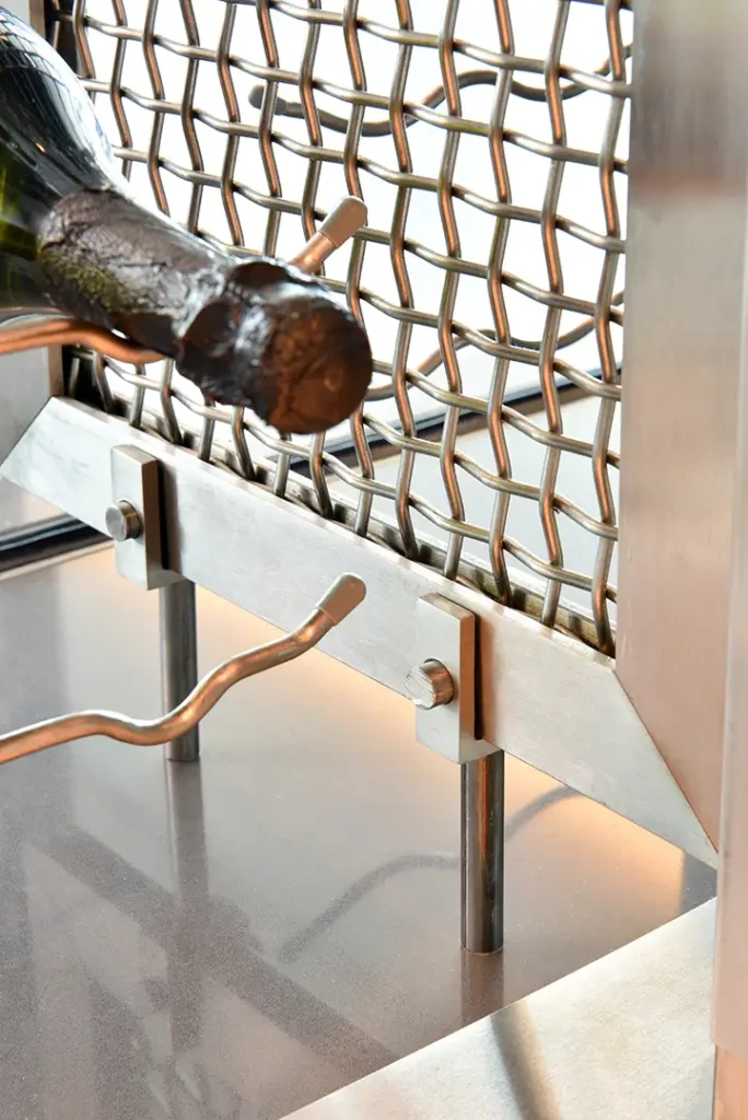 A dark wine bottle rests against metal mesh and supports in the Regalia Wine Room