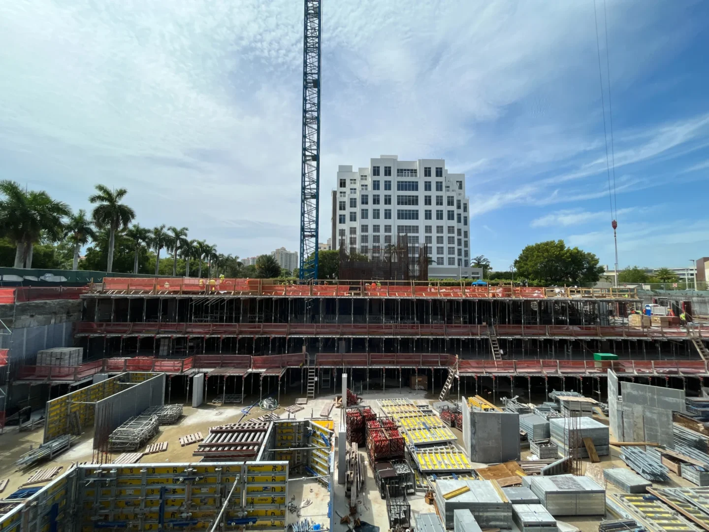 A tall blue crane stands above the multi-level scaffolding and construction materials at Safra 3050 Aventura