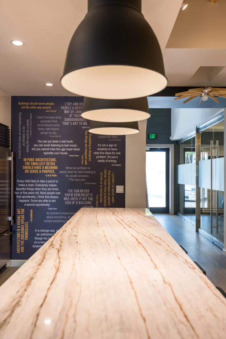 A large black pendant lamp hangs above a marble-topped counter and wall with text at ODP Architecture & Design Headquarters