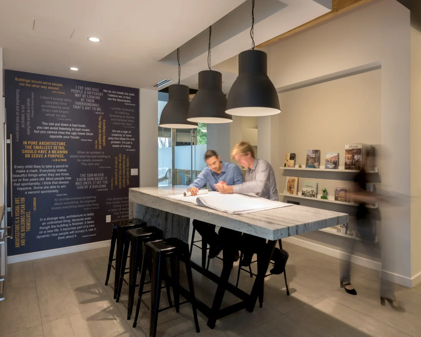 Three black pendant lights hang above men reviewing architectural drawings at ODP Architecture & Design Headquarters