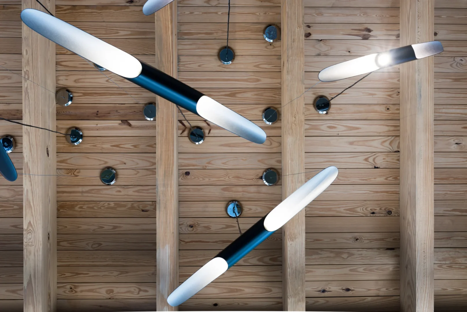 Long, white and black light fixtures hang from a wooden beam ceiling in ODP Architecture & Design Headquarters