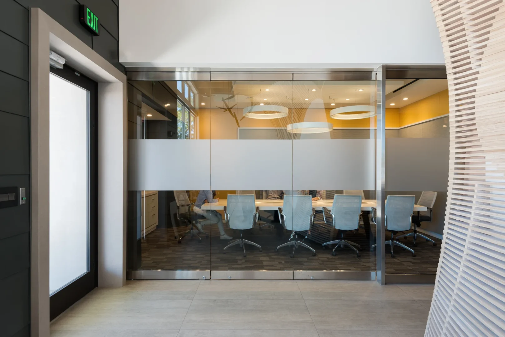 A glass-walled conference room with people inside sits next to an exit door at the ODP Architecture & Design Headquarters