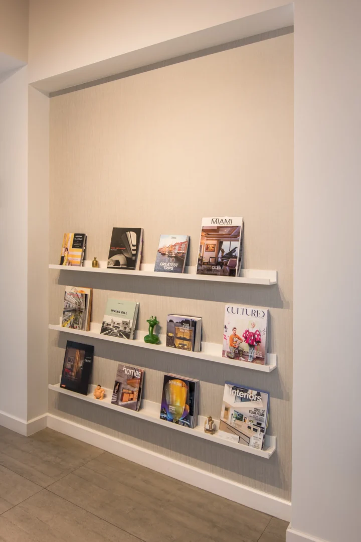 Three white floating shelves displaying magazines are mounted on a textured wall in ODP Architecture & Design Headquarters
