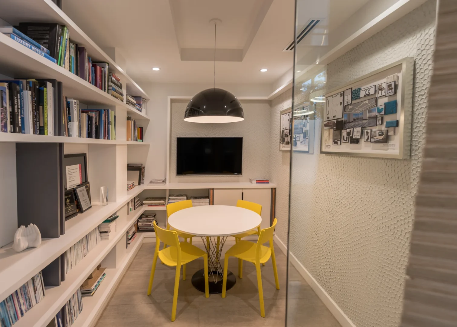 White bookshelves line a small room with a white round table and yellow chairs in ODP Architecture & Design Headquarters