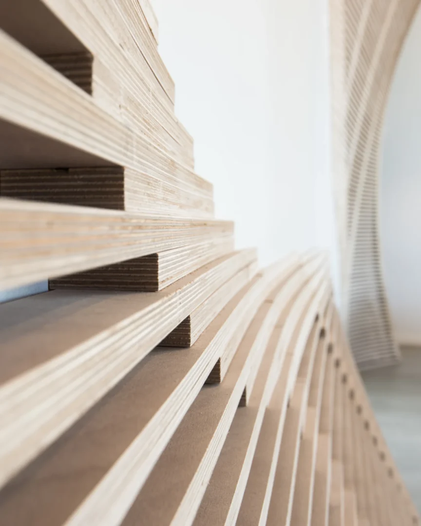 Layered plywood edges form a stepped pattern against a white wall in the ODP Architecture & Design Headquarters