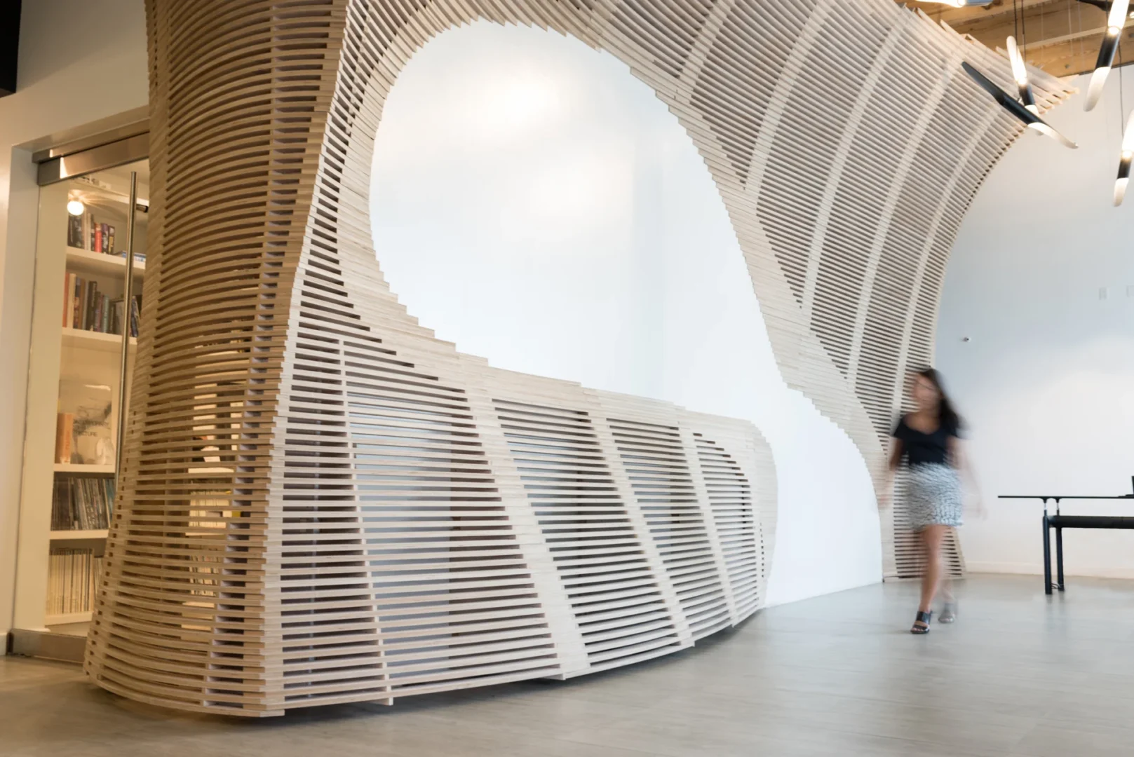 Curved wooden slats feature in the ODP Architecture & Design Headquarters near a person walking and a black table