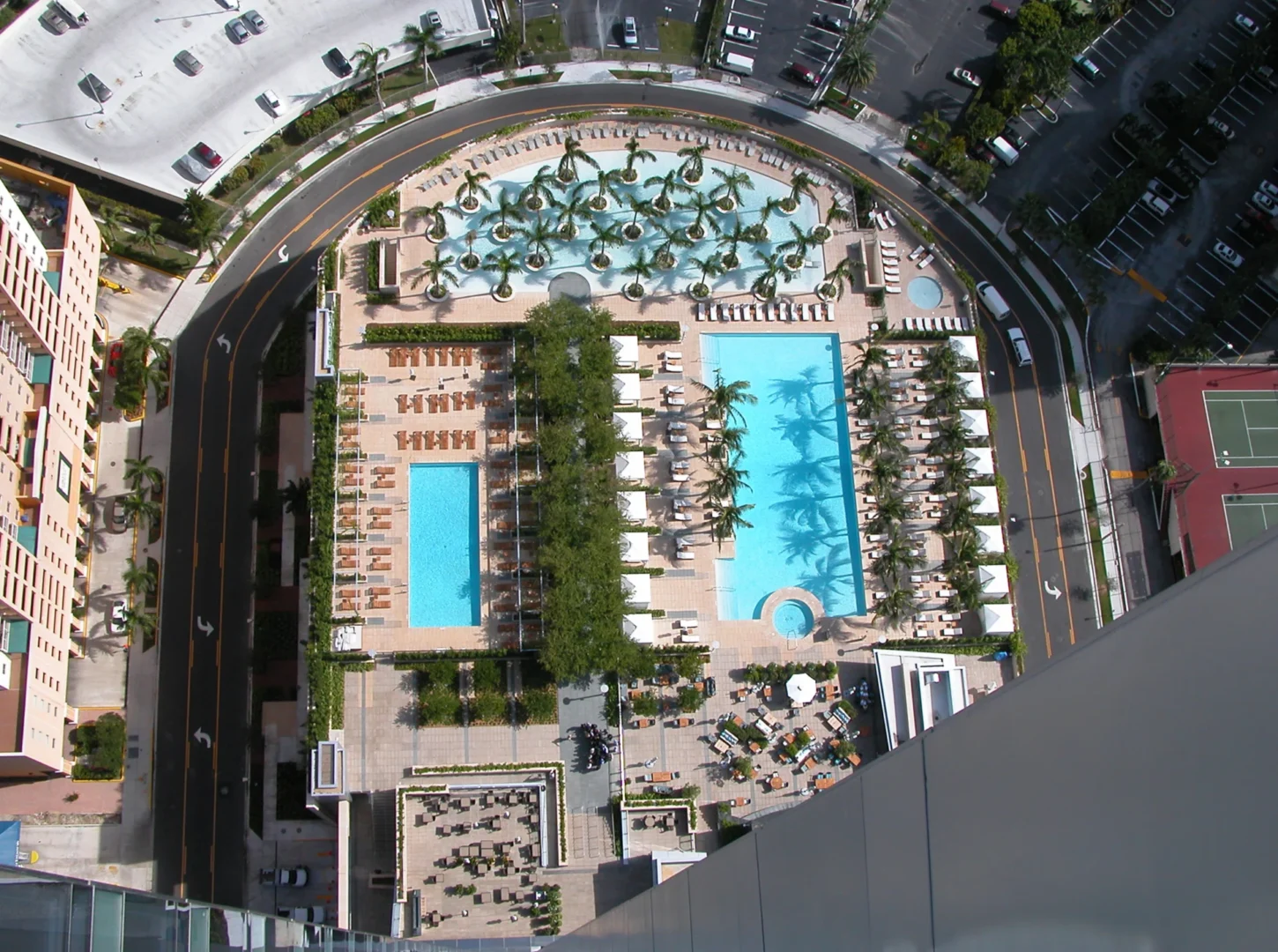 Blue swimming pools and palm trees at Naples Beach Four Seasons Resort & Residences are bordered by curved roads and parking lots