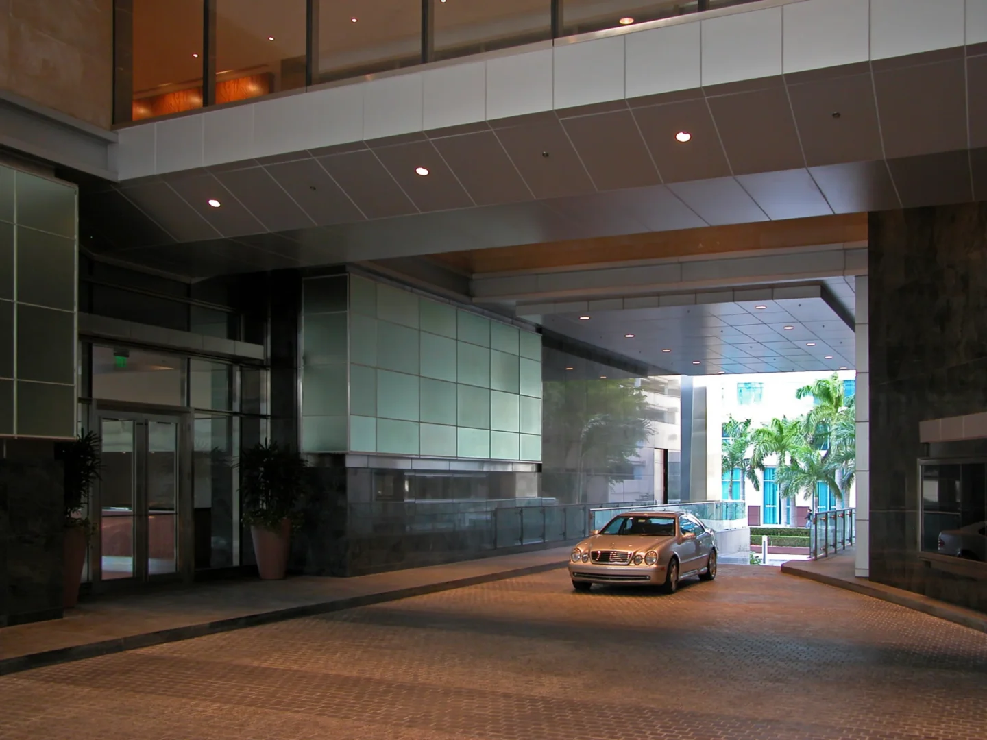 A silver car is parked on a paved driveway beneath an architectural overhang at the Naples Beach Four Seasons Resort & Residences