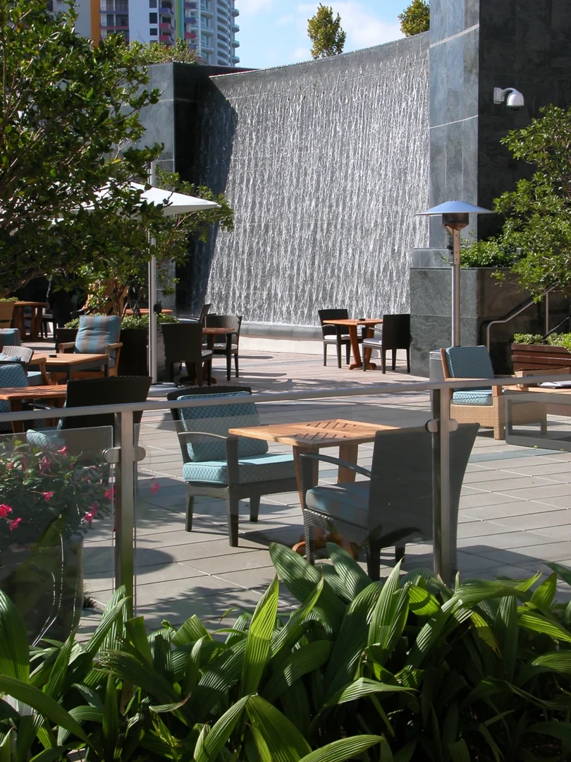A water wall stands behind an outdoor seating terrace at Naples Beach Four Seasons Resort & Residences