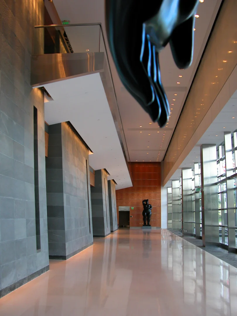 A large dark sculpture hangs above a polished hallway with grey stone walls in the Naples Beach Four Seasons Resort & Residences