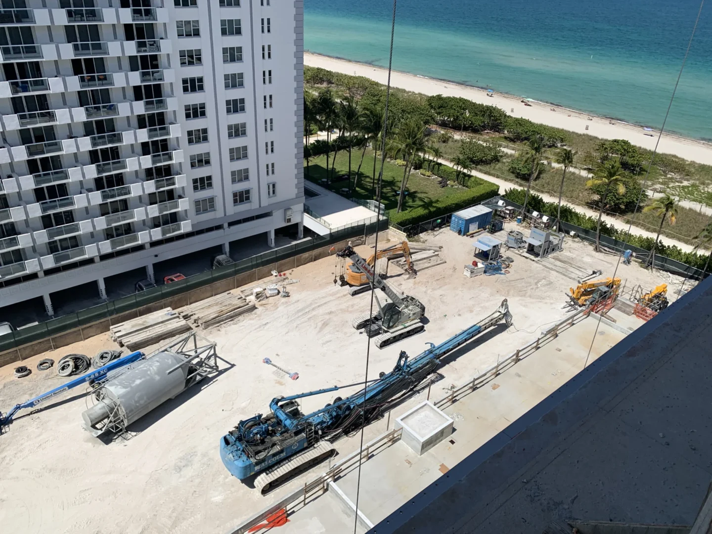 En la obra de Hillcrest, cerca de una playa junto al mar, hay un rascacielos blanco y maquinaria pesada.