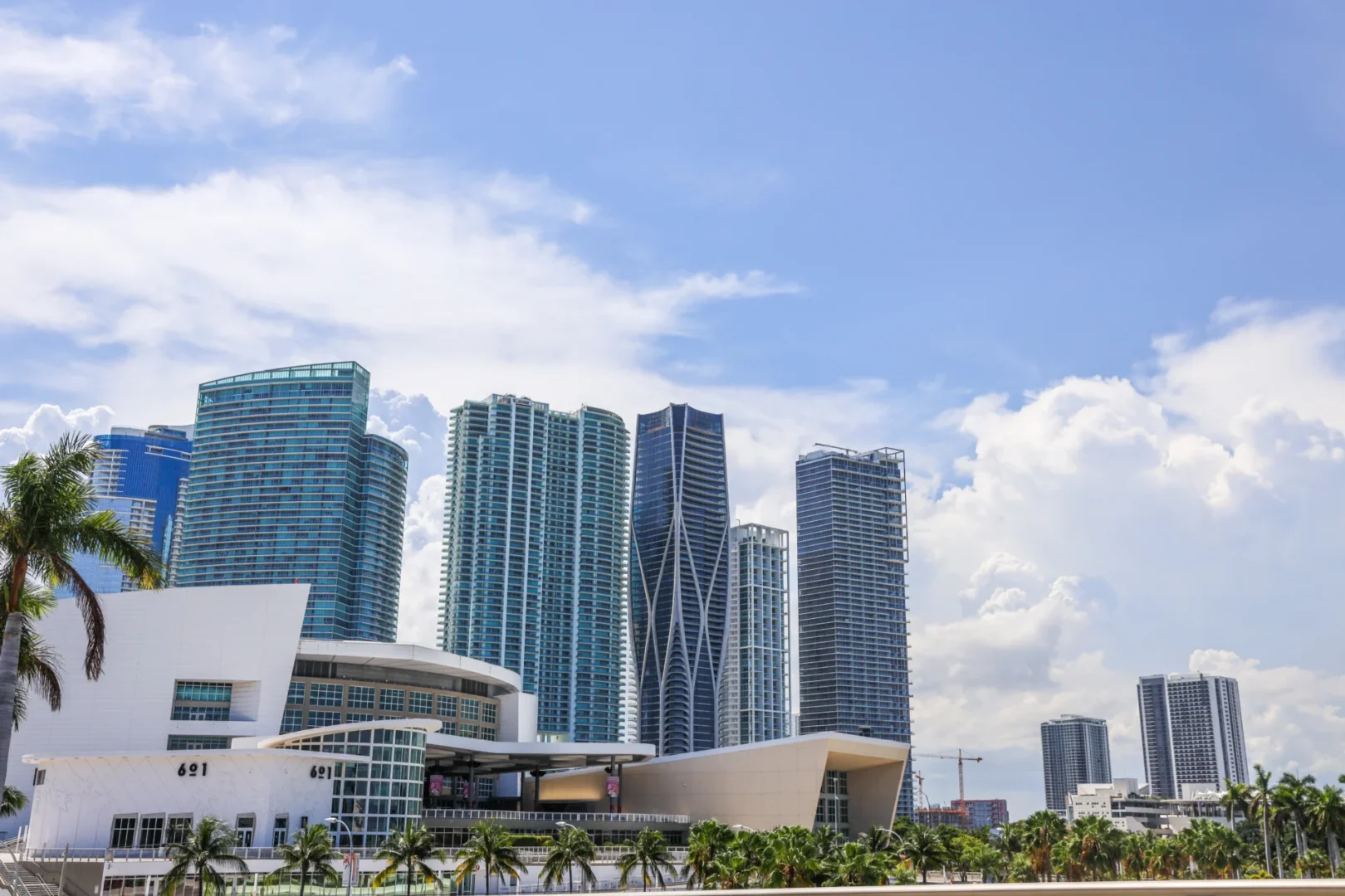 Skyscrapers including One Thousand Museum rise against a cloudy blue sky above palm trees and white buildings