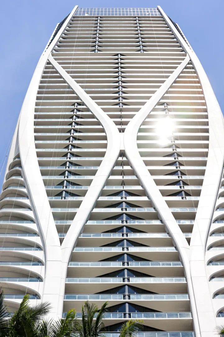 White, curved structural ribs of One Thousand Museum rise above palm trees under a blue sky