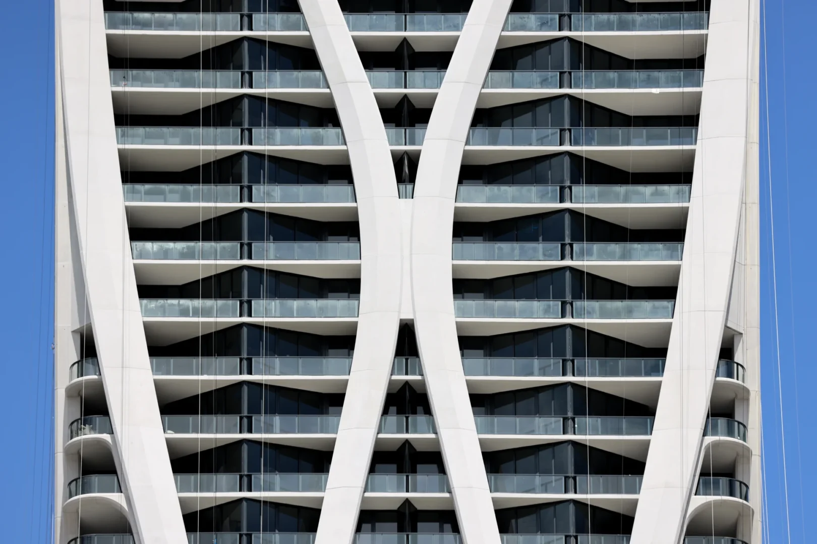 White curved structural elements pattern dark glass balconies on One Thousand Museum against a blue sky