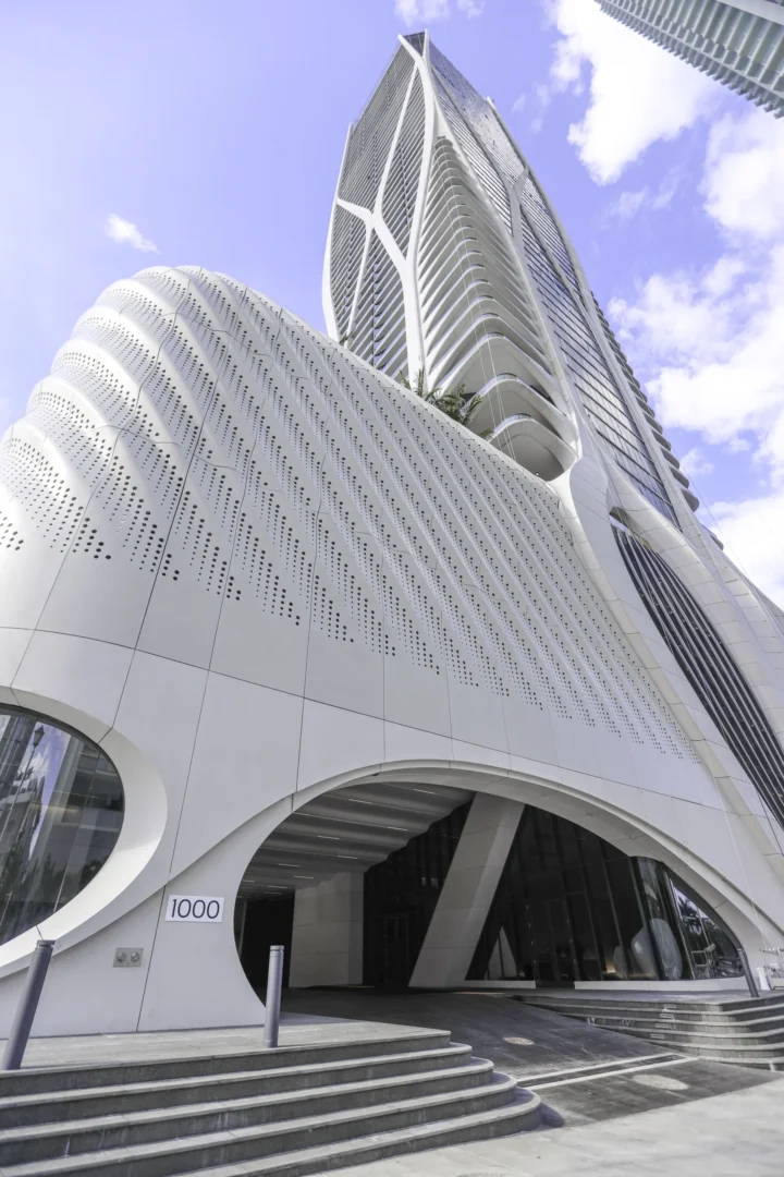 A white, textured skyscraper in One Thousand Museum features a curved base and concrete steps leading toward an entrance