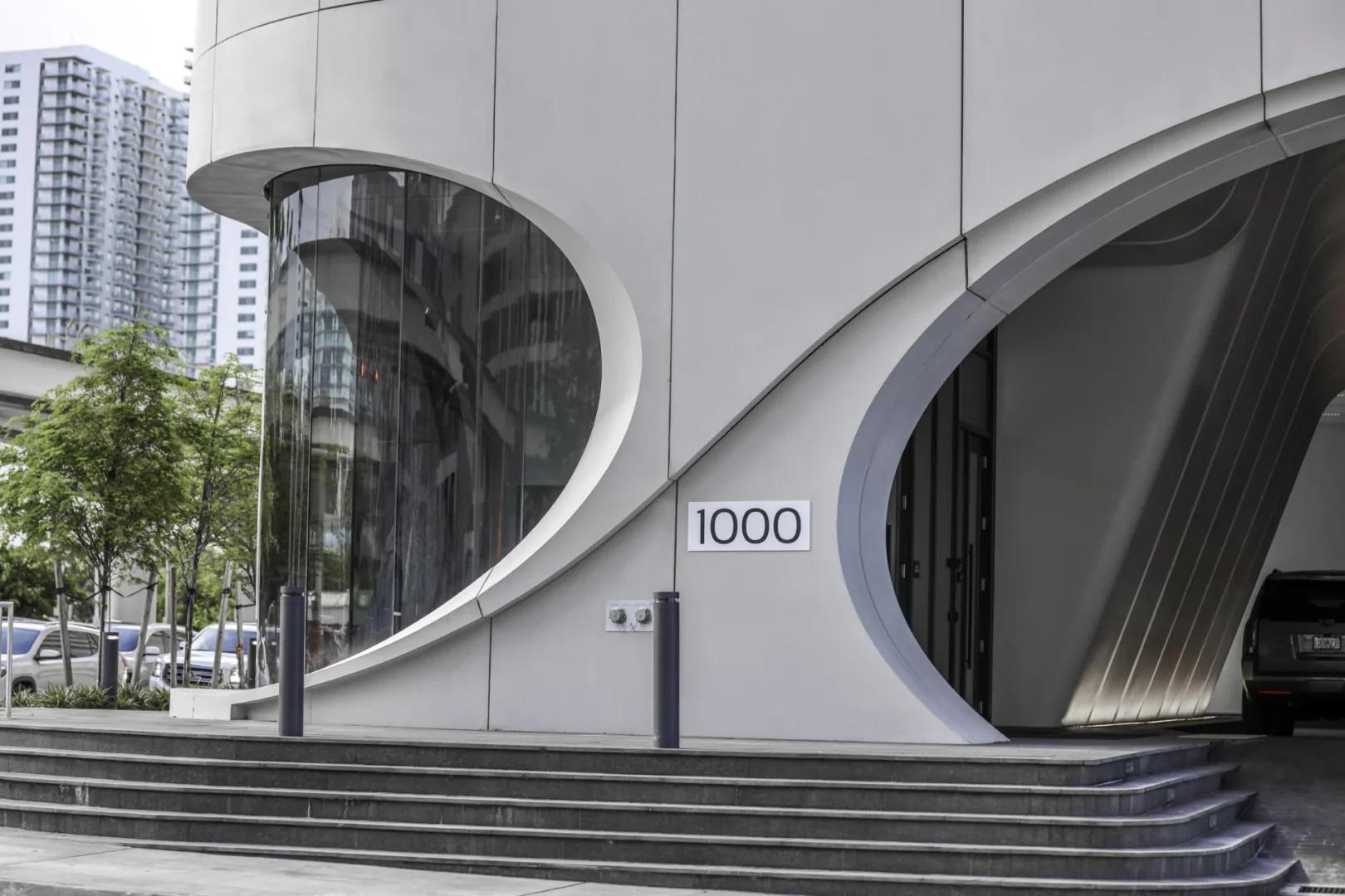 Curved white panels of One Thousand Museum feature large glass windows, a sign reading 1000, and concrete steps