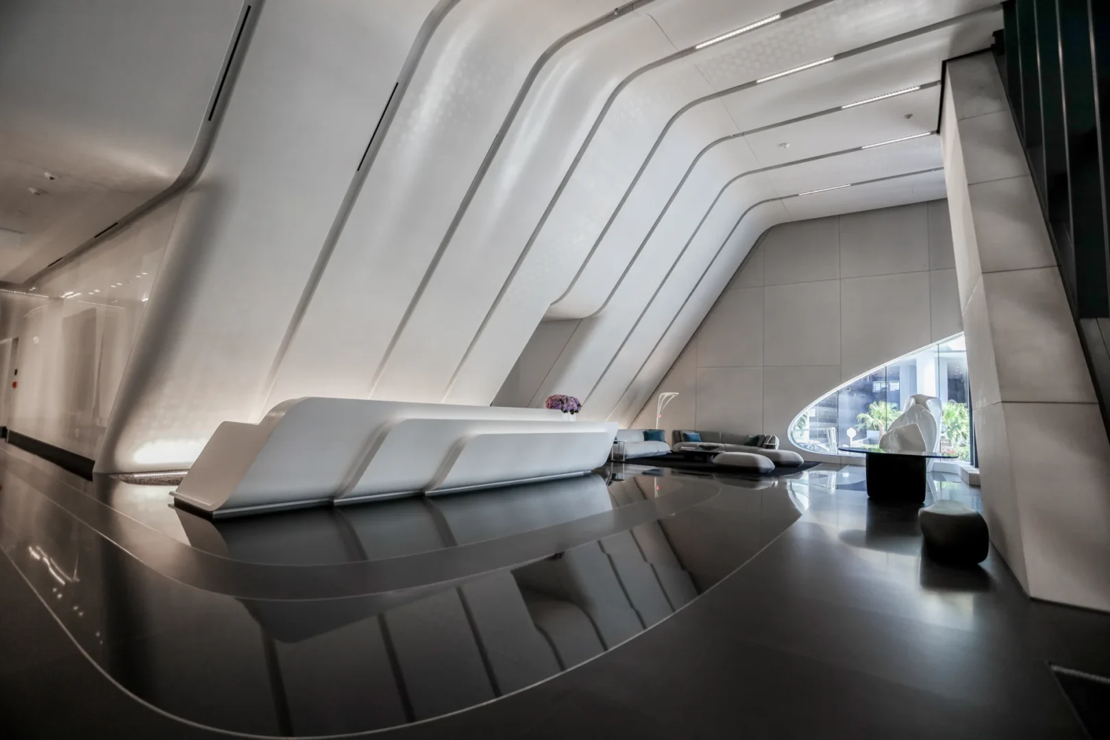 White curved architectural features surround a white reception desk on a dark reflective floor in the One Thousand Museum lobby