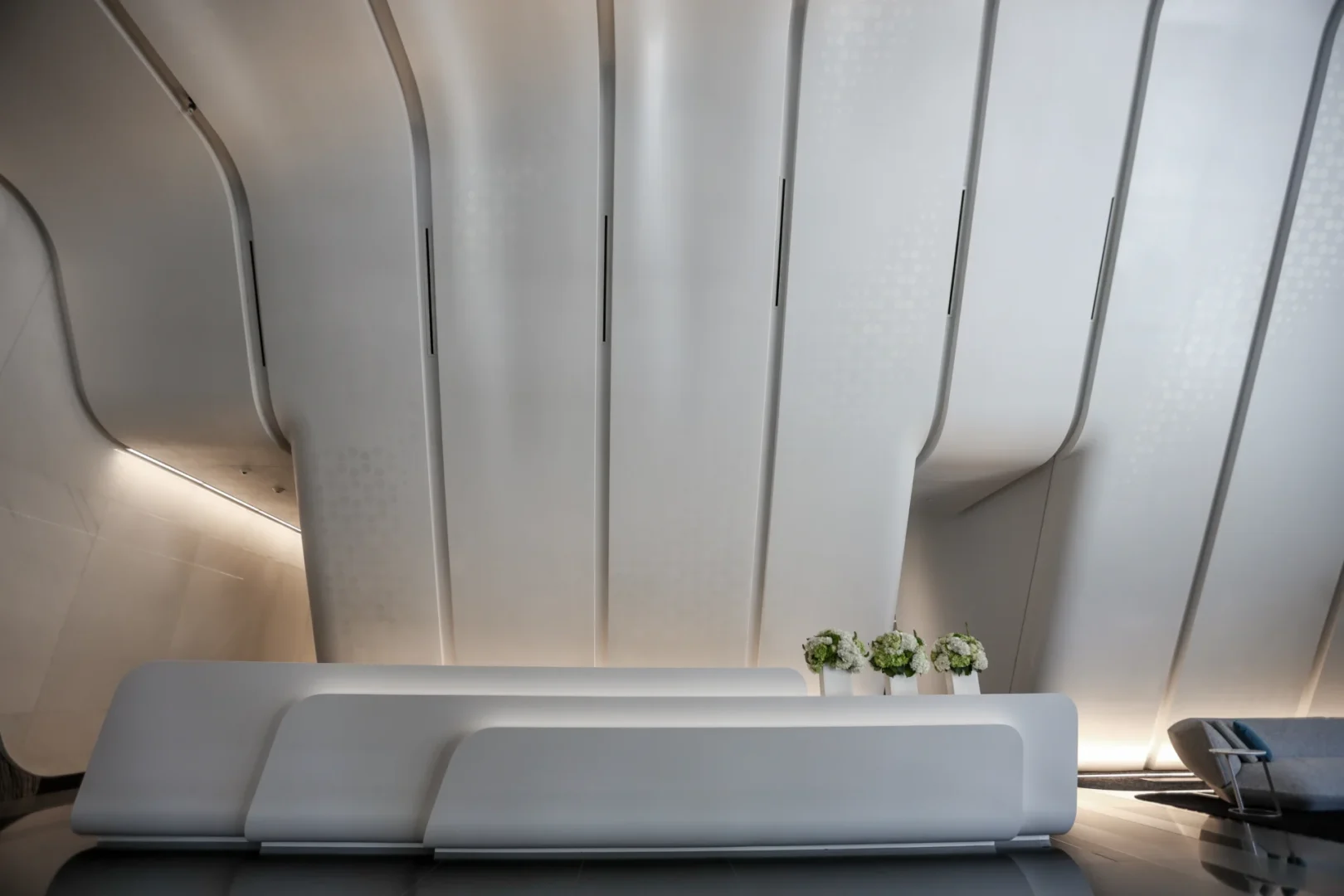 White curved vertical panels at One Thousand Museum stand behind a long white counter with small floral arrangements