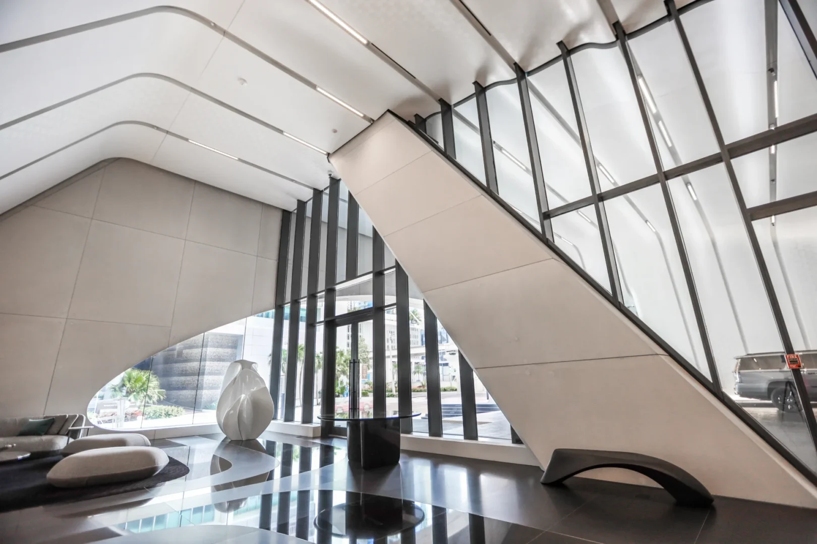 An angular white structure and floor-to-ceiling windows overlook a street from the One Thousand Museum lobby