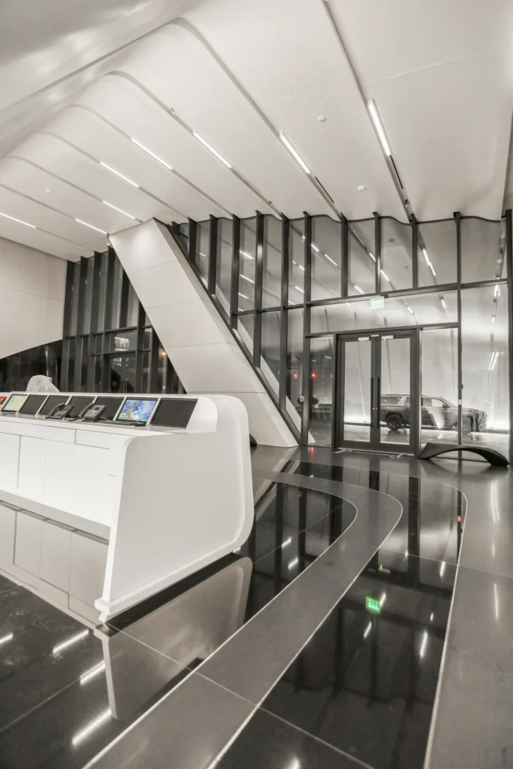 A white curved reception desk stands in the One Thousand Museum lobby near large glass walls and a polished black floor