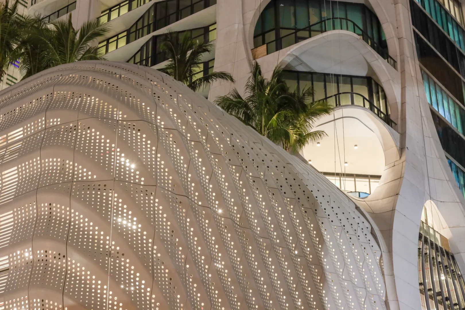 A white perforated structure at One Thousand Museum sits near palm trees and glass windows