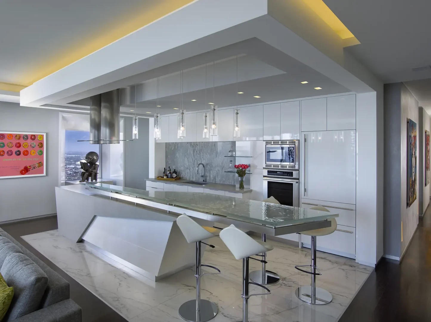 A white kitchen island with a glass countertop and bar stools sits under an architectural soffit in Penthouse 1
