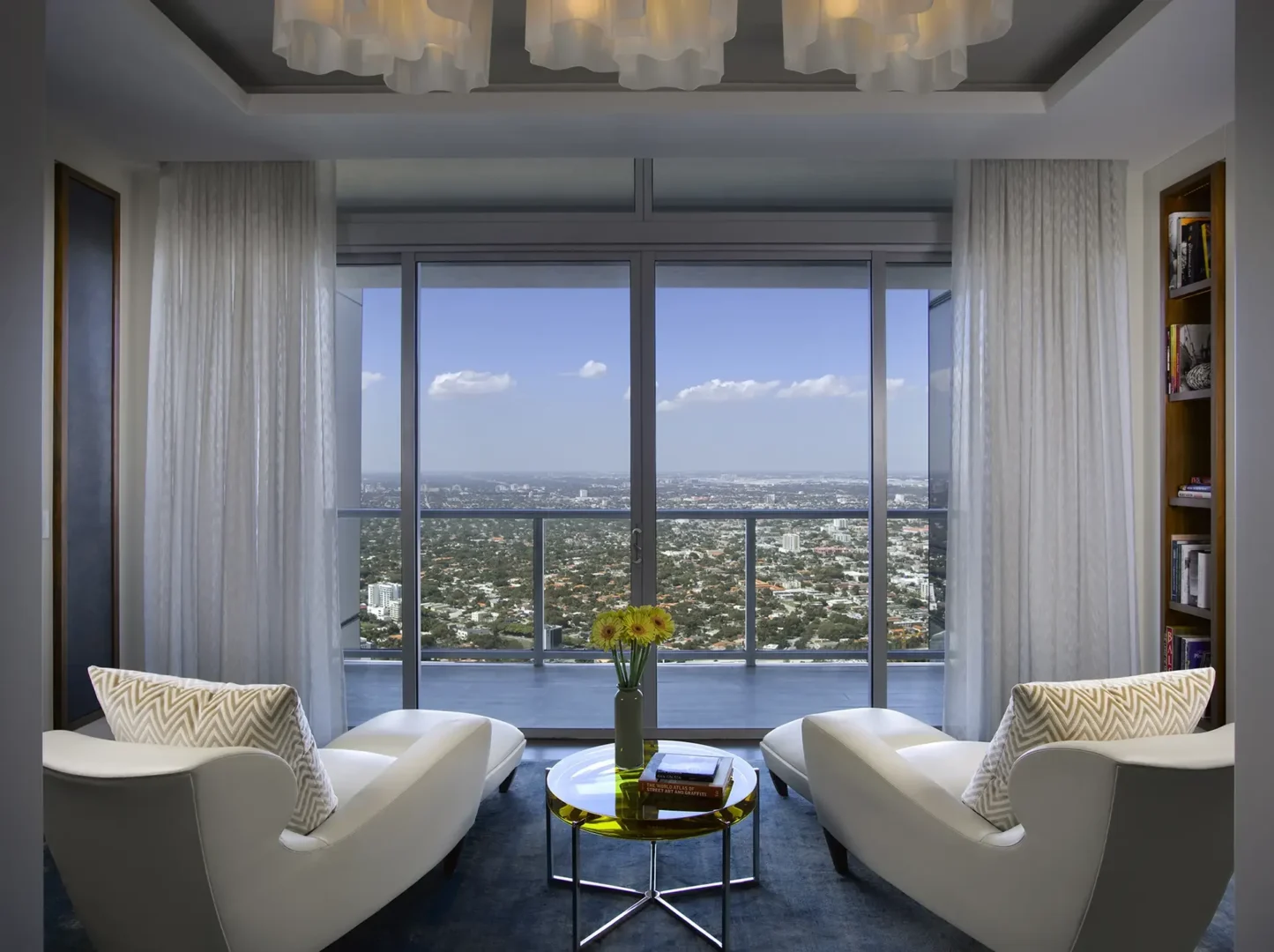 Two white armchairs face a small coffee table in the Penthouse 1 living area, looking out at a cityscape through large windows