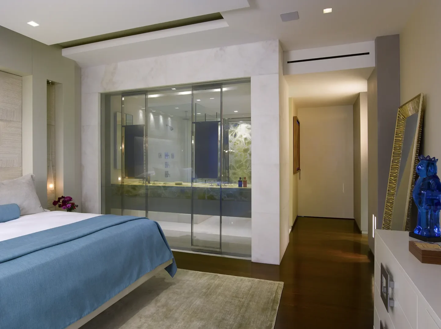 A blue bed in Penthouse 1 sits beside a glass-walled bathroom and an adjacent hallway