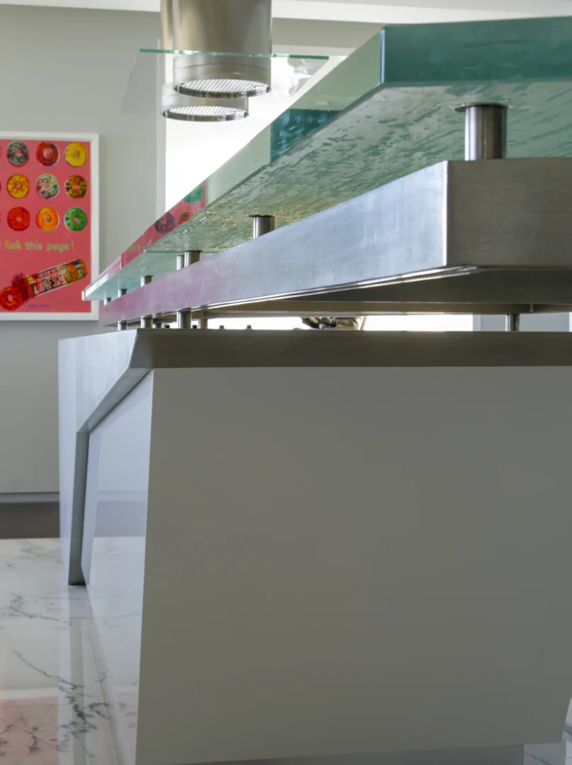 Una isla de cocina de gran grosor, con encimera de cristal y bordes metálicos, forma parte del ático 2