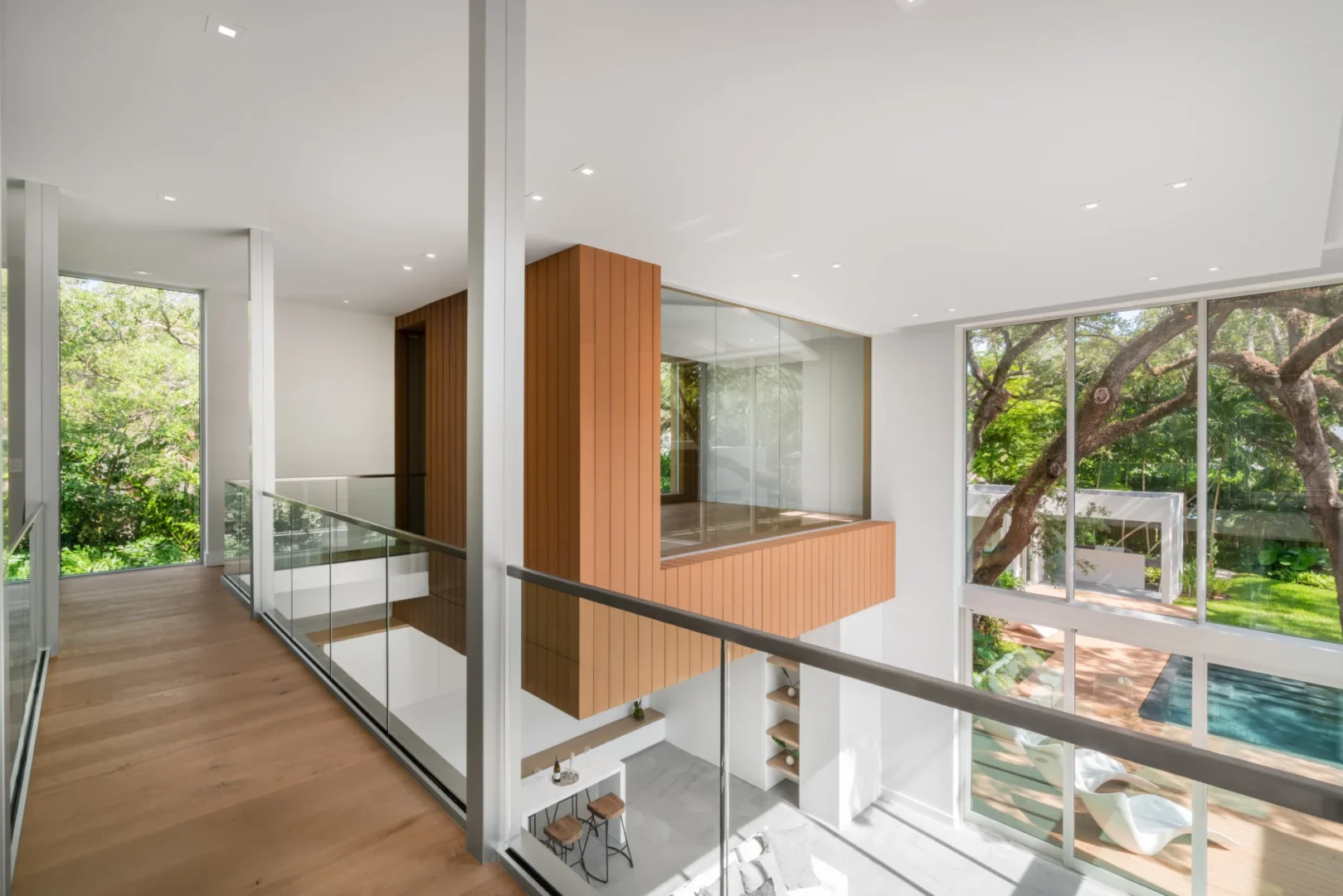 A wood-clad structure in the multi-level interior of South Miami Residence is surrounded by glass railings and large windows
