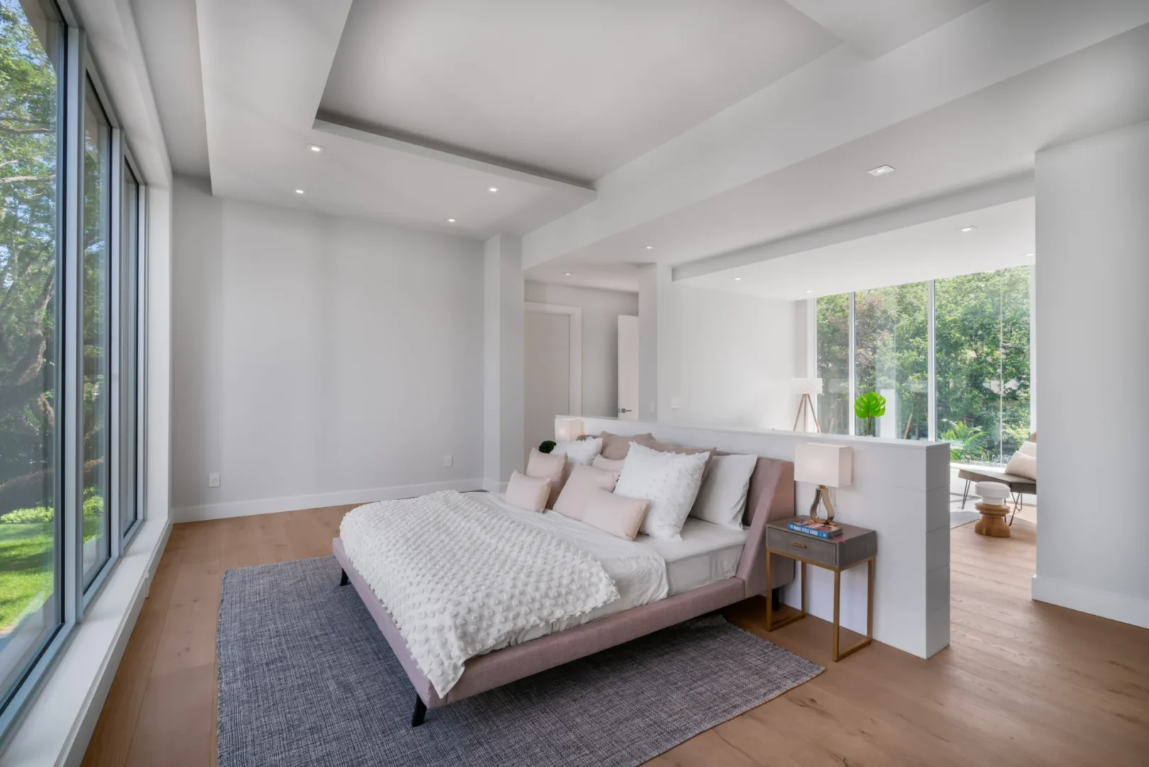 A bed with white bedding sits on a grey rug in a South Miami Residence bedroom with large windows and wood floors