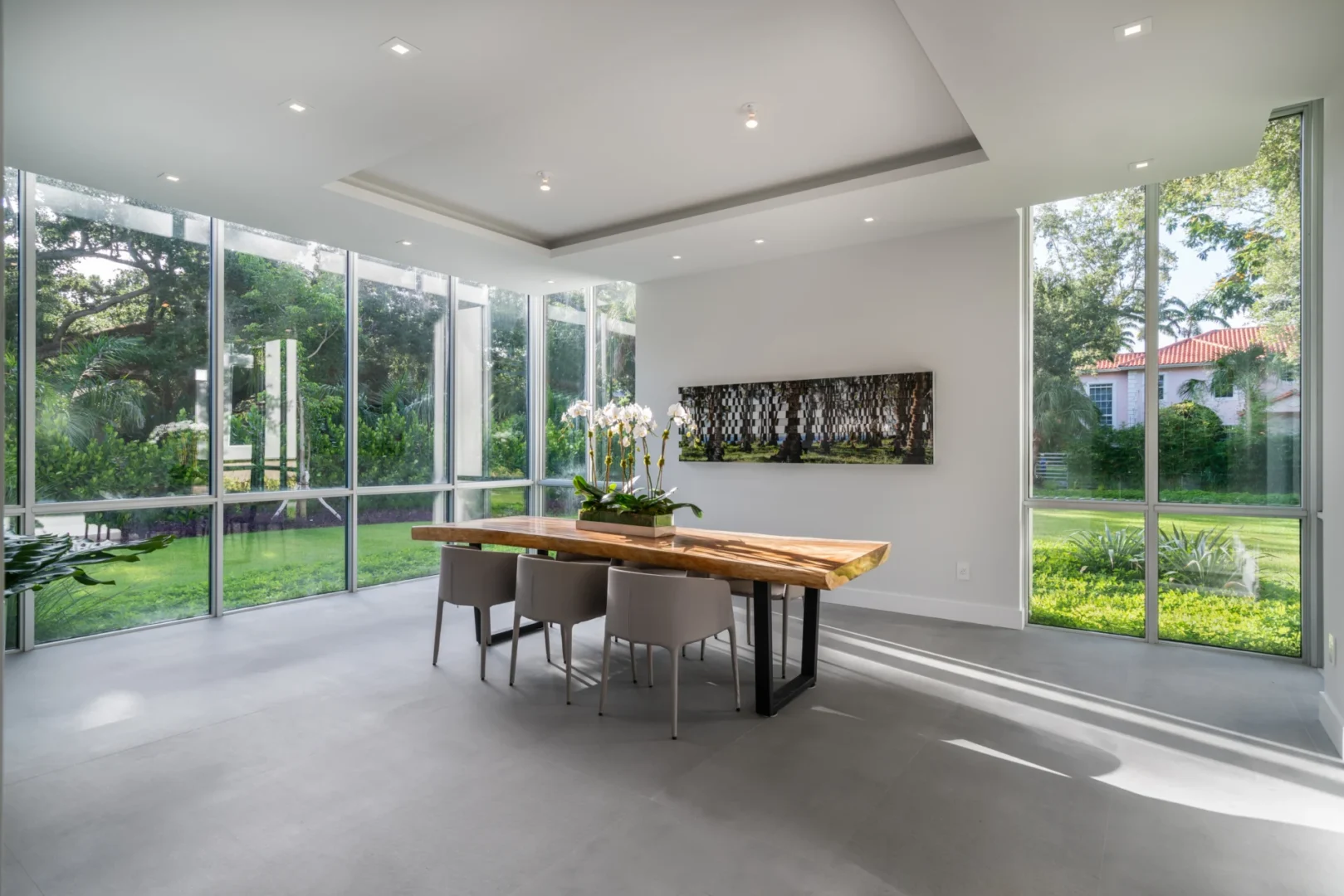 A wooden dining table and grey chairs are in a glass-walled dining room of the South Miami Residence