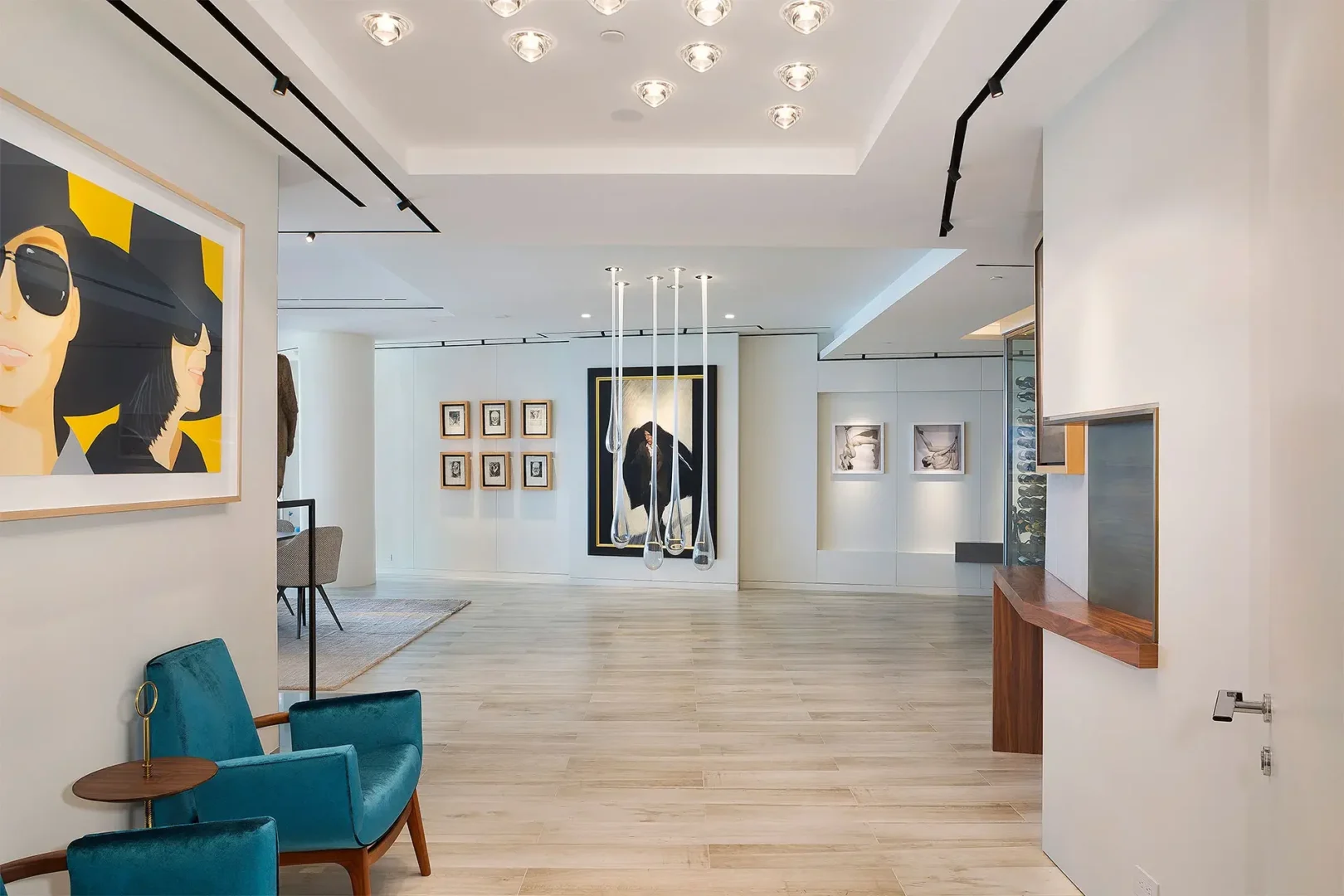 Framed paintings are displayed on white walls in a Surfside Seaway interior with blue armchairs and track lighting