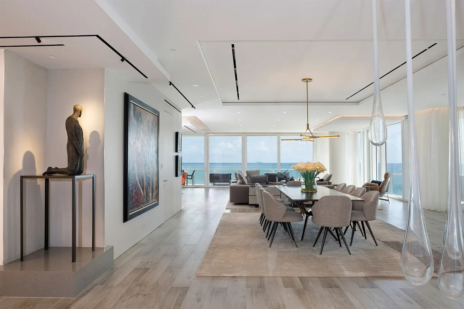 An open dining and living area in Surfside Seaway includes a dark table, grey chairs, and large windows overlooking the ocean