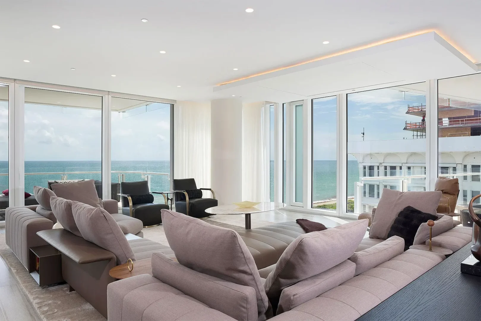Neutral-toned sofas and armchairs are in a Surfside Seaway living room with large windows overlooking the ocean