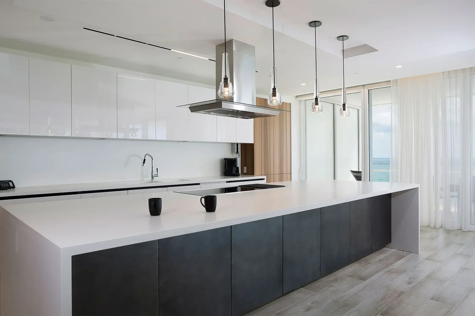 A large white kitchen island with dark cabinetry is in the Surfside Seaway kitchen overlooking the ocean through glass doors
