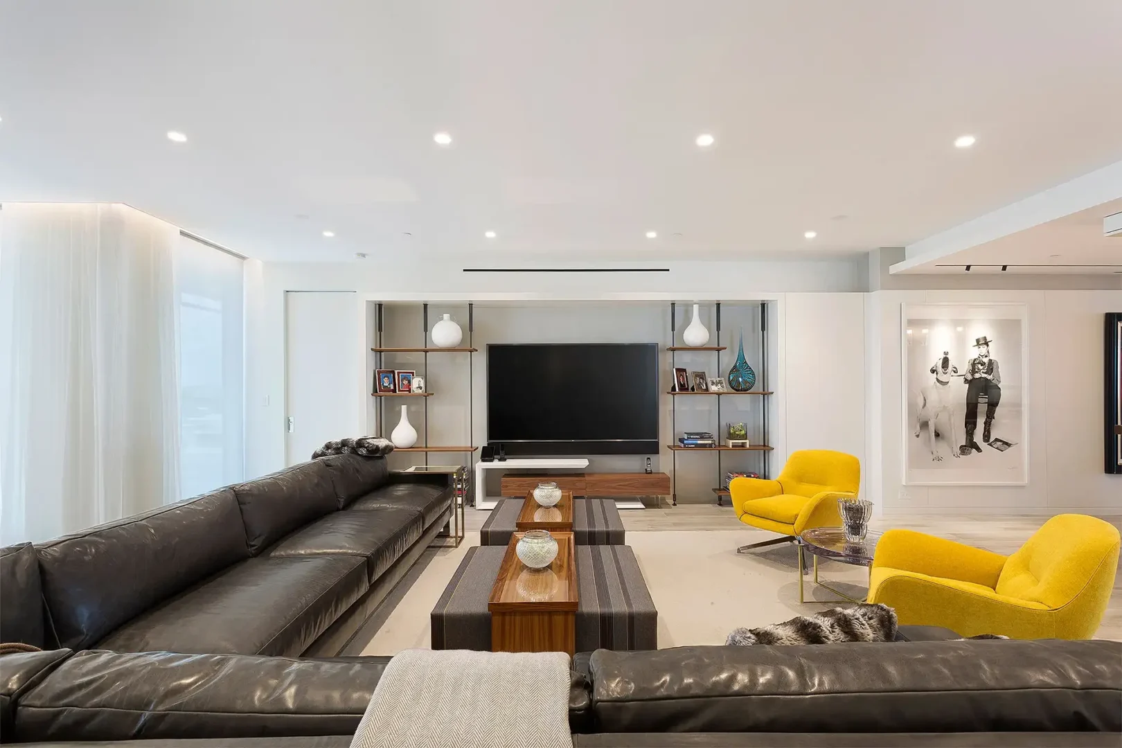 A large dark leather sofa and two yellow armchairs are in the Surfside Seaway living room near a television unit