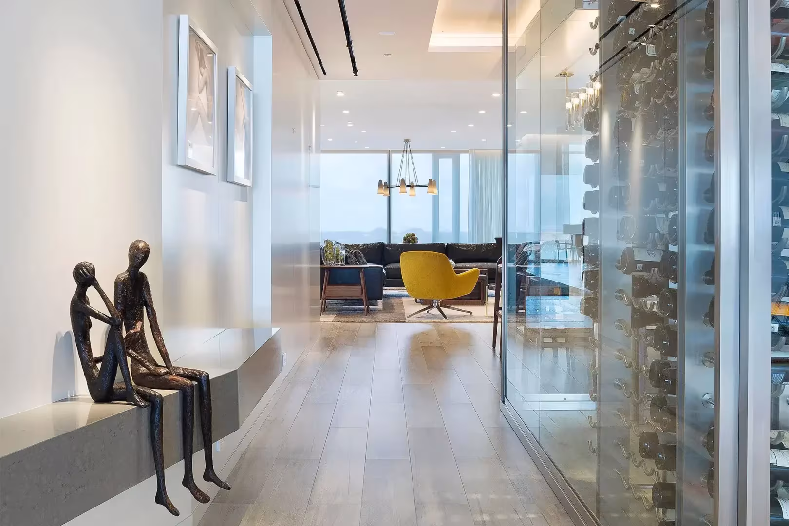 A glass-enclosed wine display lines a hallway with metal sculptures leading into a living room at Surfside Seaway