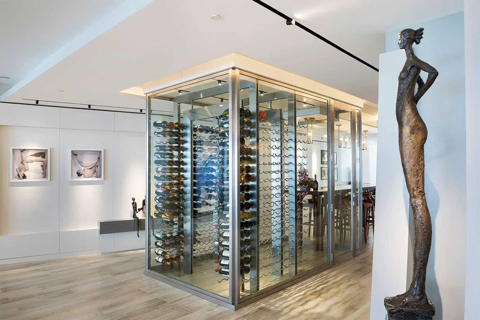 A glass-enclosed wine cellar with numerous bottles stands in the Surfside Seaway interior beside a tall bronze sculpture