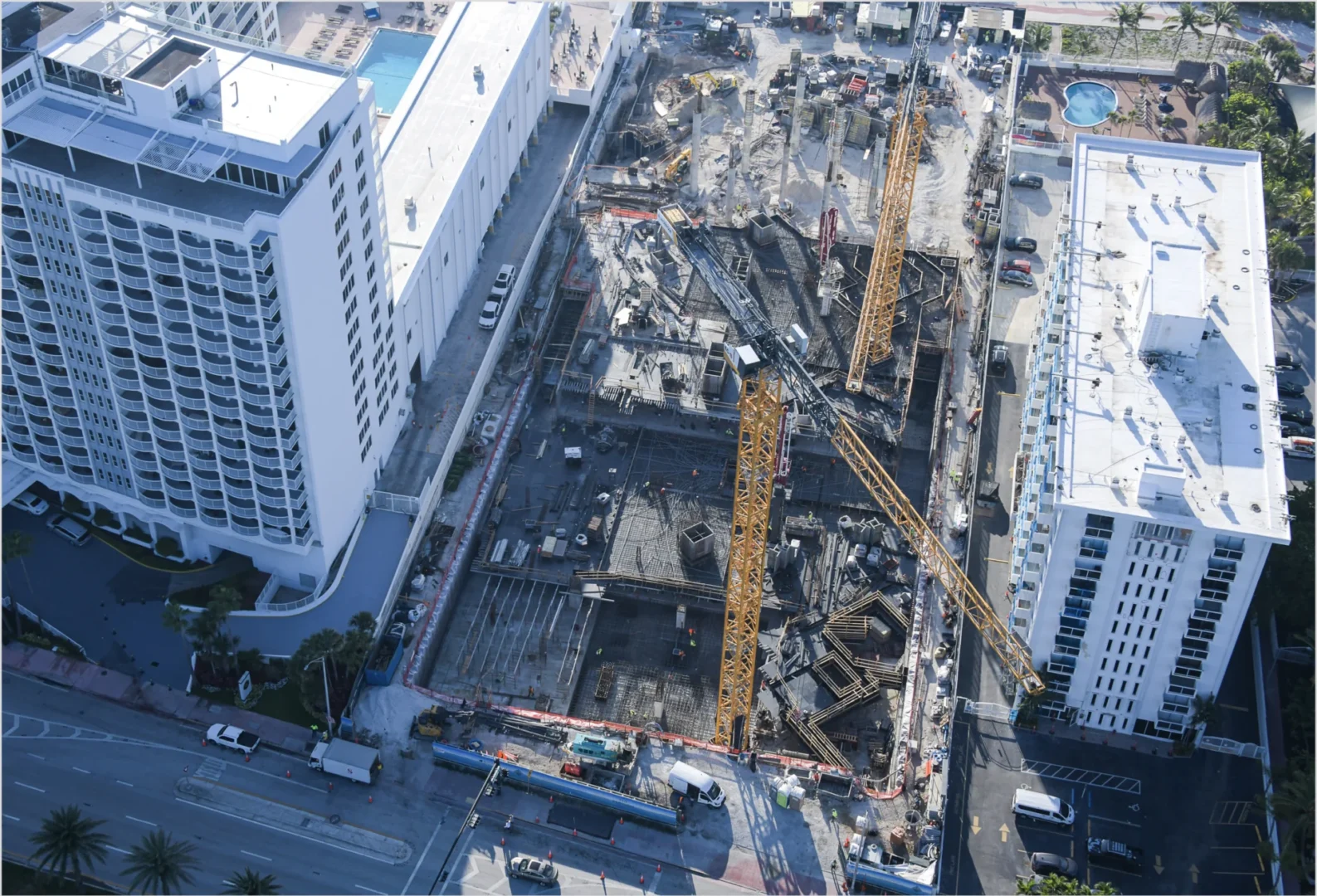 Yellow cranes stand over a construction site for The Perigon among white multi-story buildings and paved streets