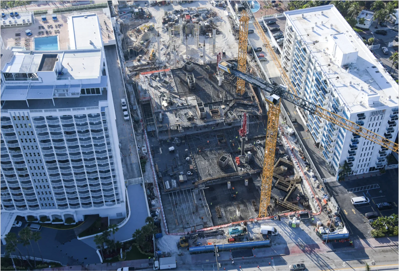 Yellow cranes and workers are visible at The Perigon construction site between large white buildings