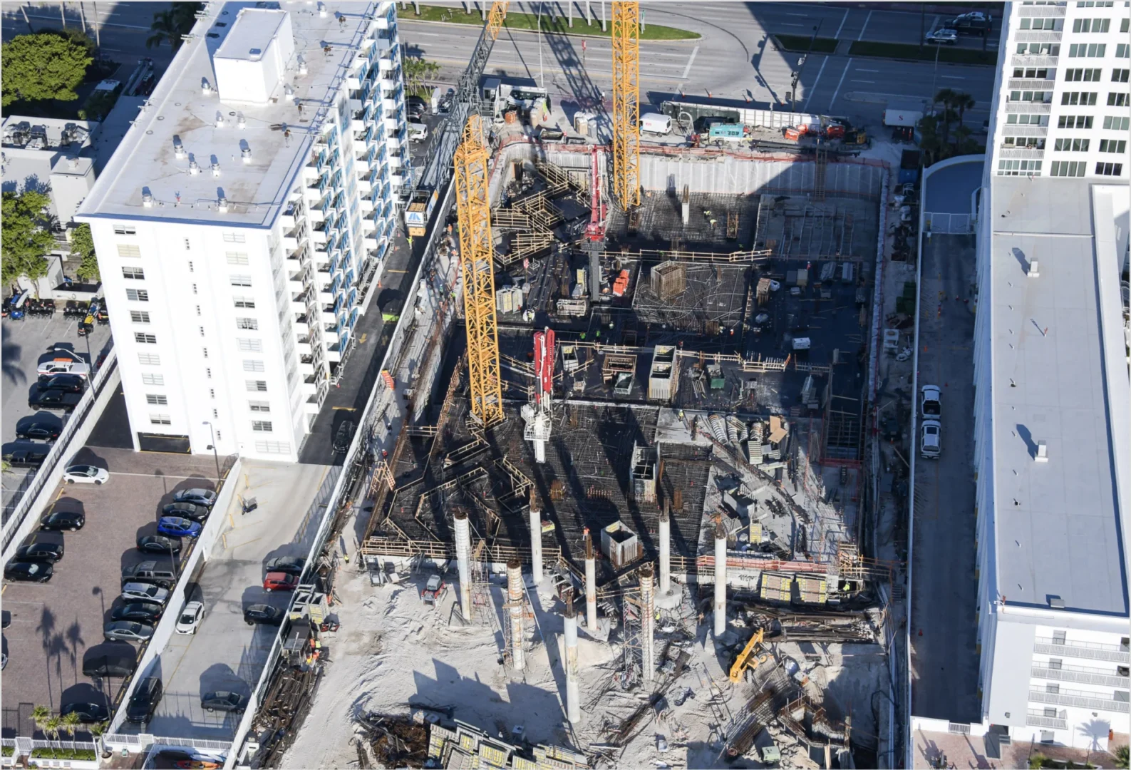 Large yellow cranes stand over a construction site for The Perigon featuring concrete columns and rebar