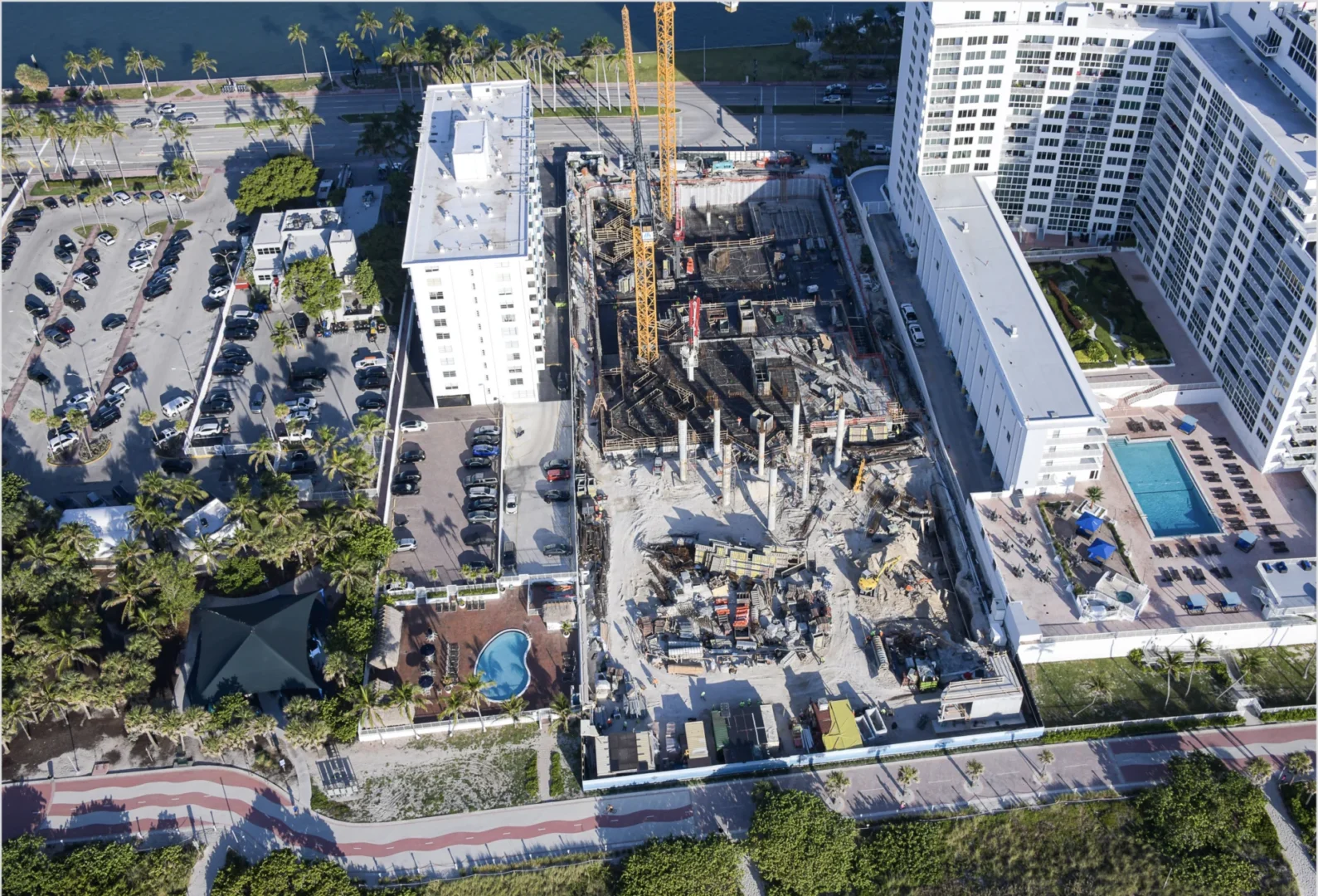 Yellow cranes rise above the construction site at The Perigon, flanked by high-rise buildings and parking lots