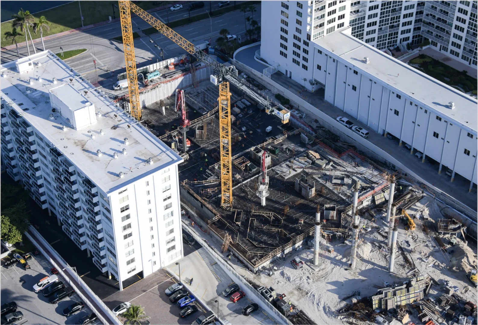 Yellow cranes and structural work for The Perigon are located between several large white buildings