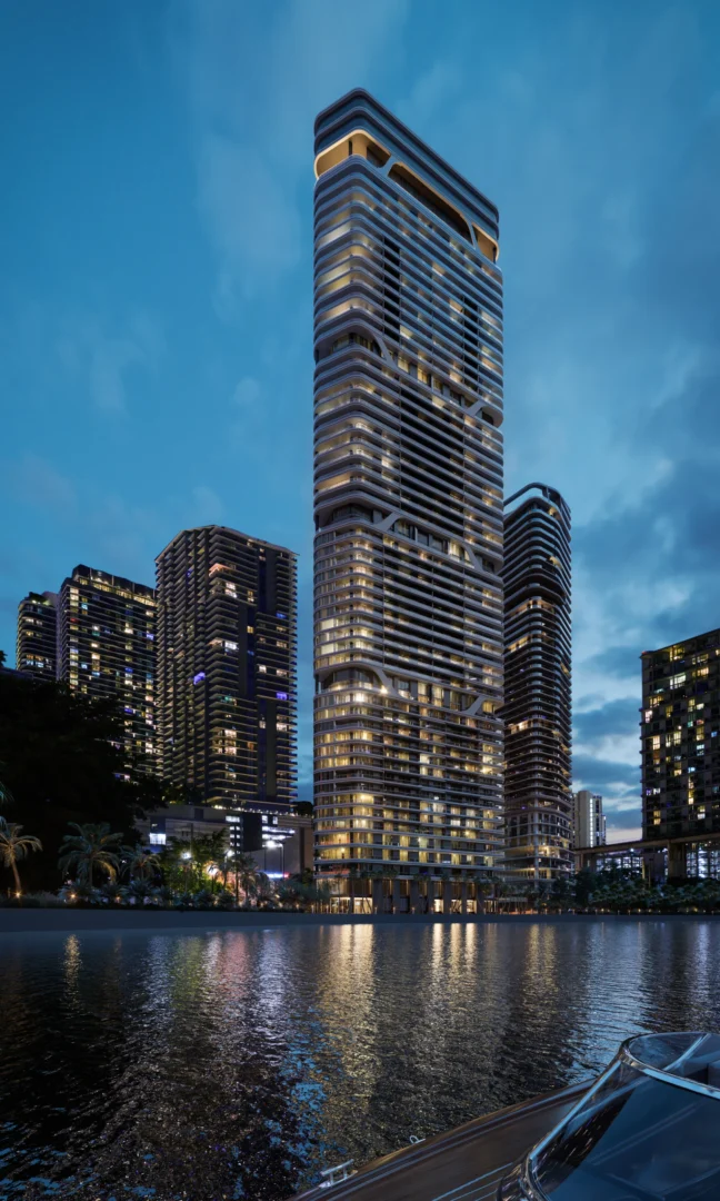 A tall skyscraper in Two Riverside rises among other high-rise buildings beside water reflecting lights