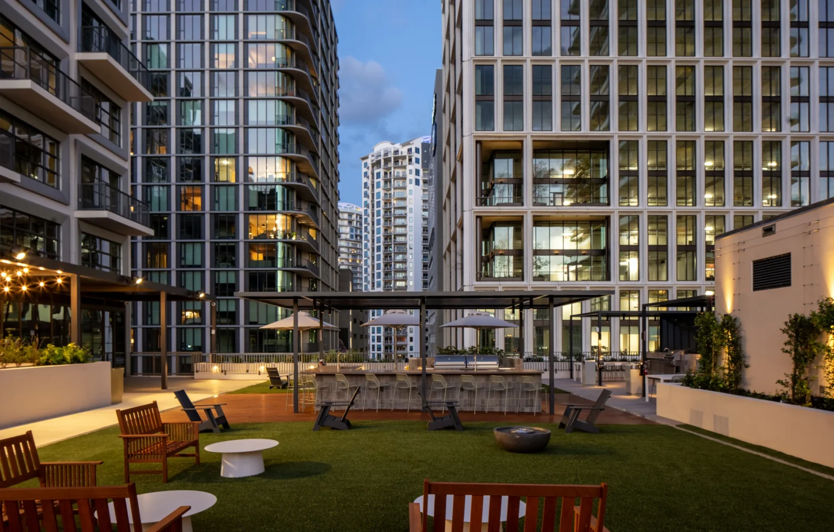 La terraza al aire libre del Asher Water Street Tampa está rodeada de edificios altos y cuenta con sillones y una zona de bar cubierta.