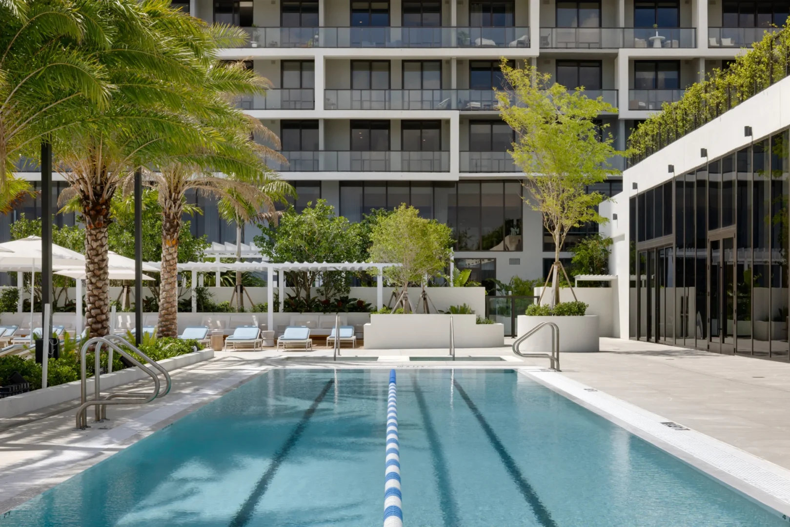 A swimming pool with blue and white lane markers sits in front of a terrace and the balconies of the multi-story Forma building