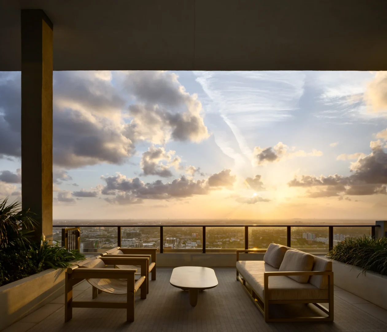 A cloudy sunset sky over a terrace in Forma with lounge seating, a coffee table, and plants overlooking a city