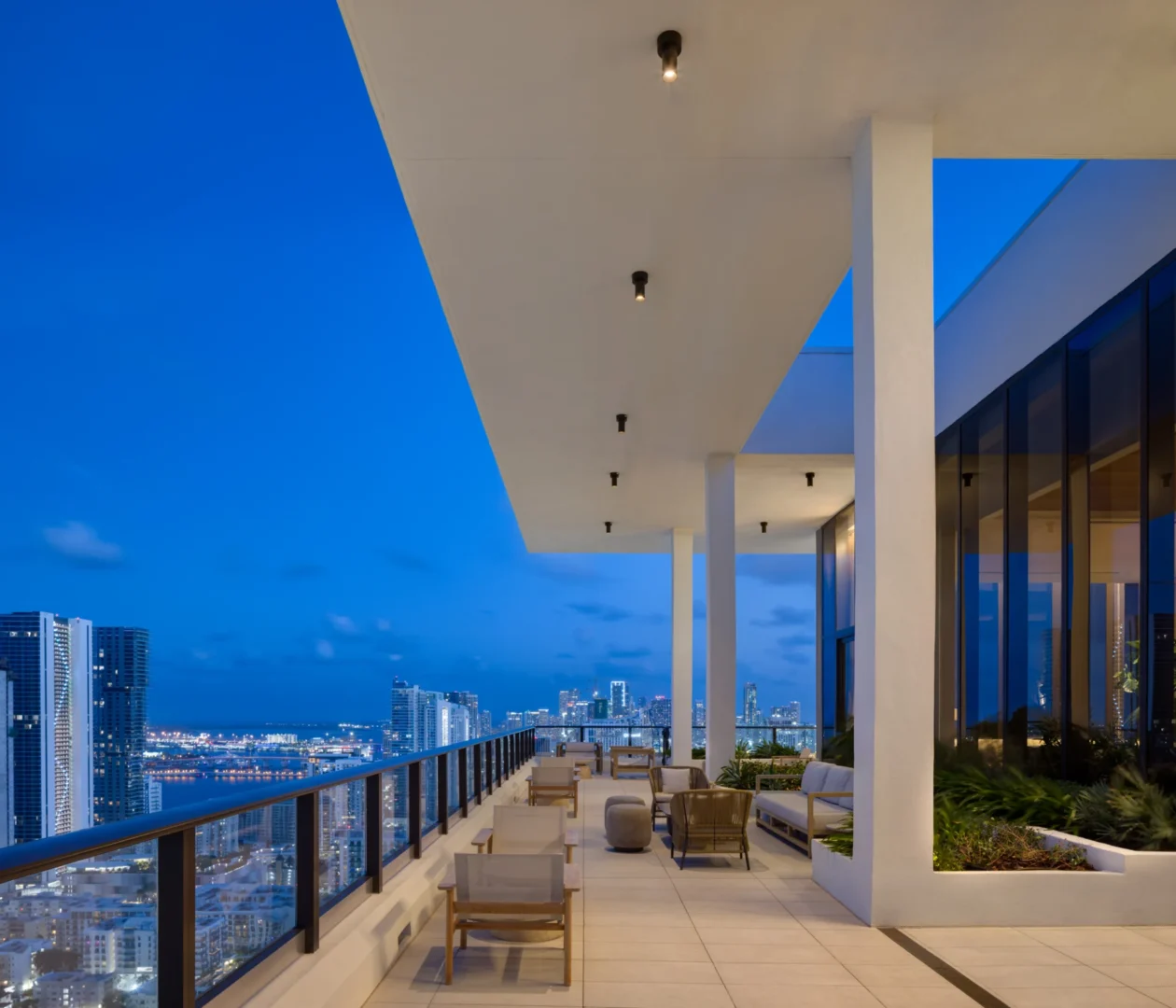 A white-columned terrace in the Forma project contains outdoor seating and overlooks a lit city skyline